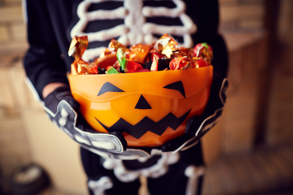 Boy in skeleton costume holding bowl full of candies for Halloween safety tips blog