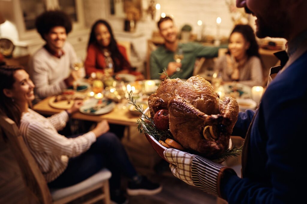 image of people around a table as someone brings a turkey for giving back to your community for thanksgiving blog post