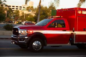 red ambulance heading down road with trees in background
